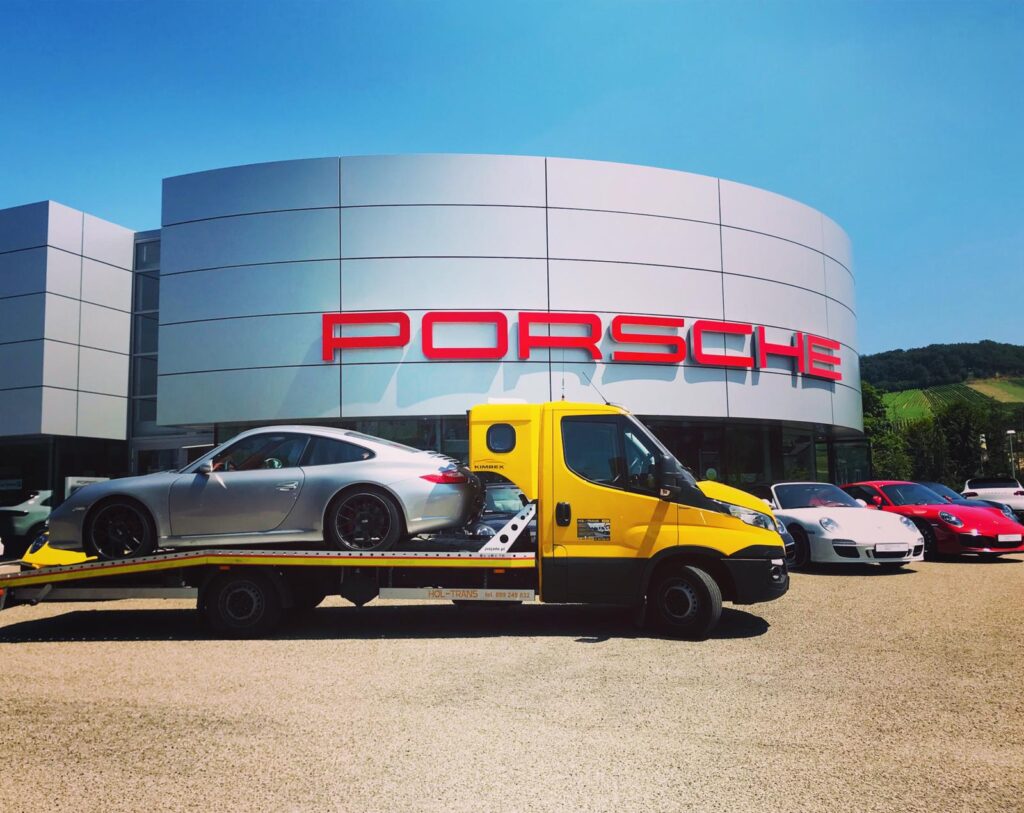 srebrny samochód na żółtej lawecie na tle salonu samochodowego